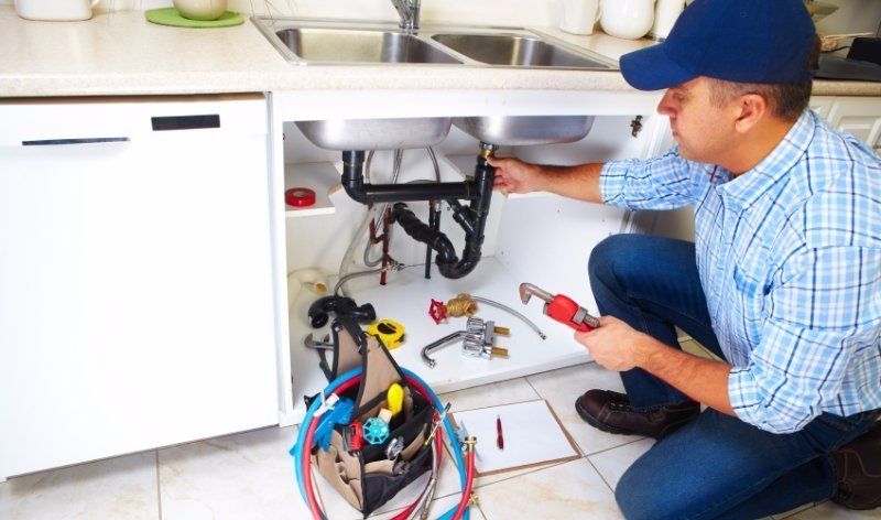 plumber fixing pipes under a sink with various plumbing tools