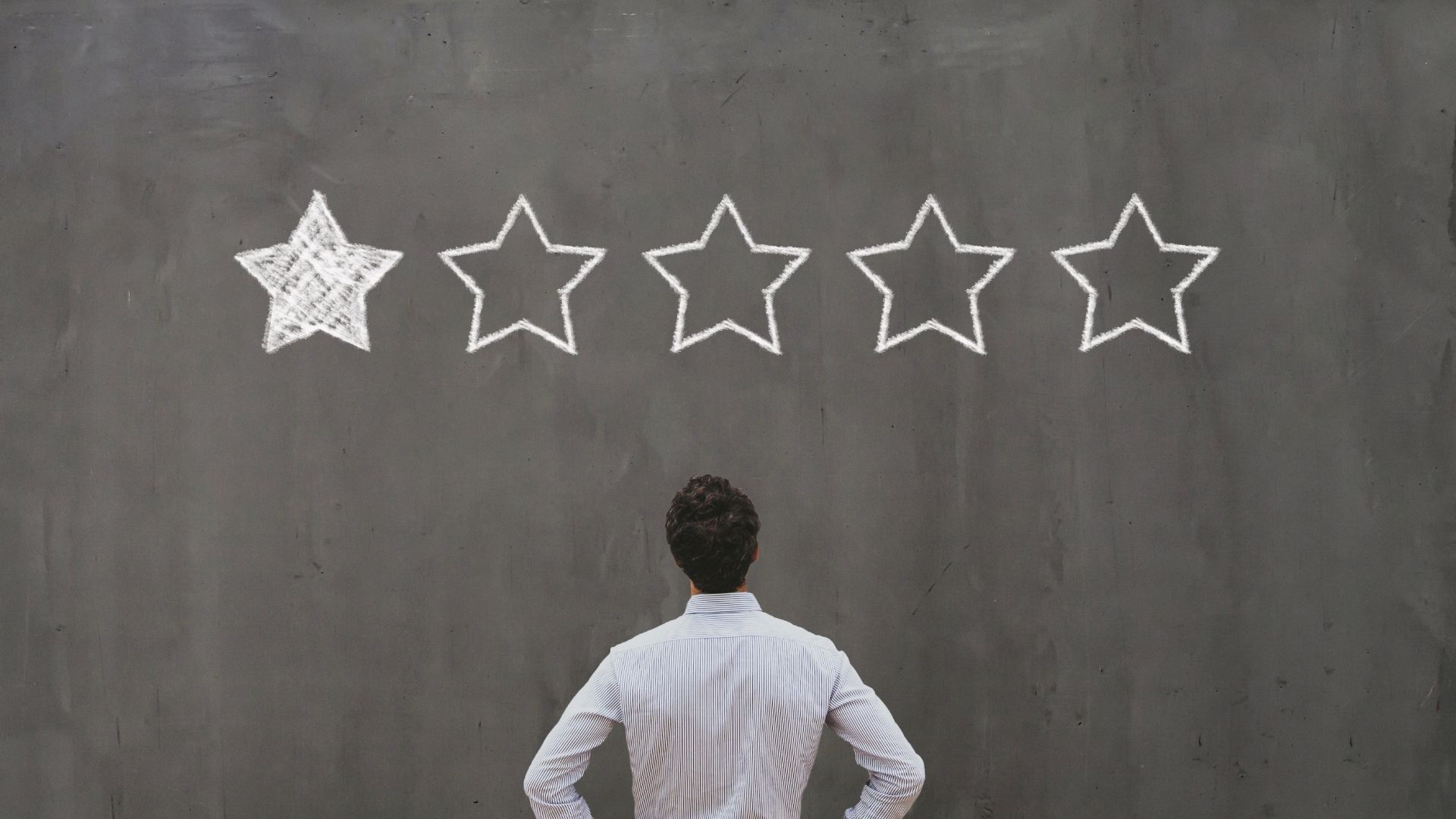 A man is standing in front of a blackboard with five stars drawn on it.