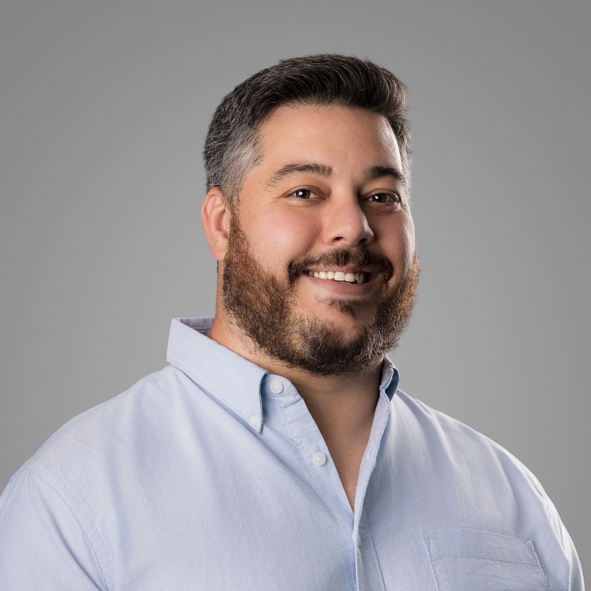 A man with a beard is wearing a blue shirt and smiling.