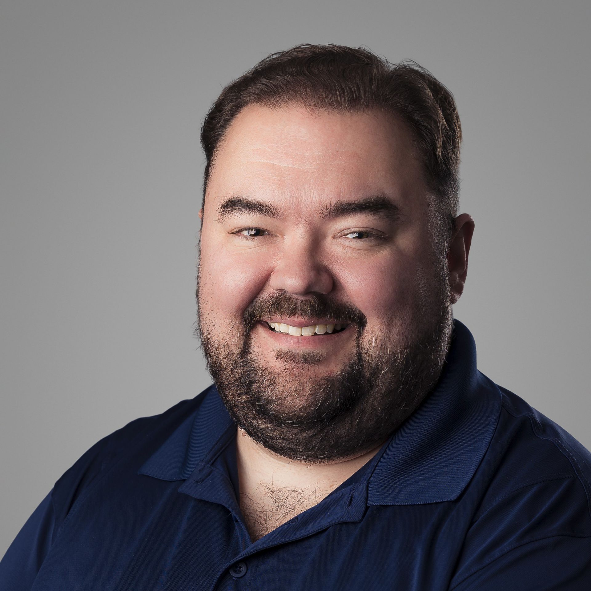A man with a beard wearing a blue shirt smiles for the camera