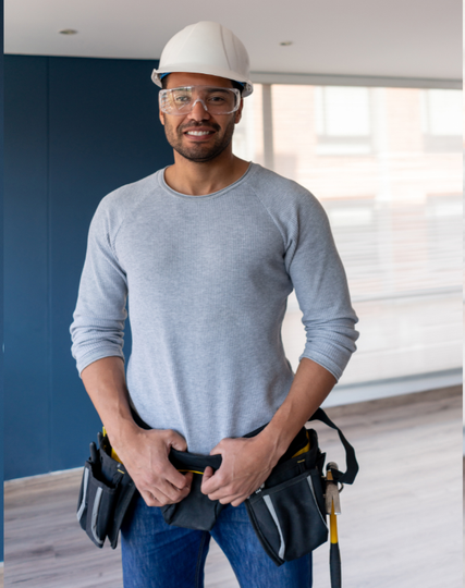 A man wearing a hard hat and goggles is standing in an empty room.