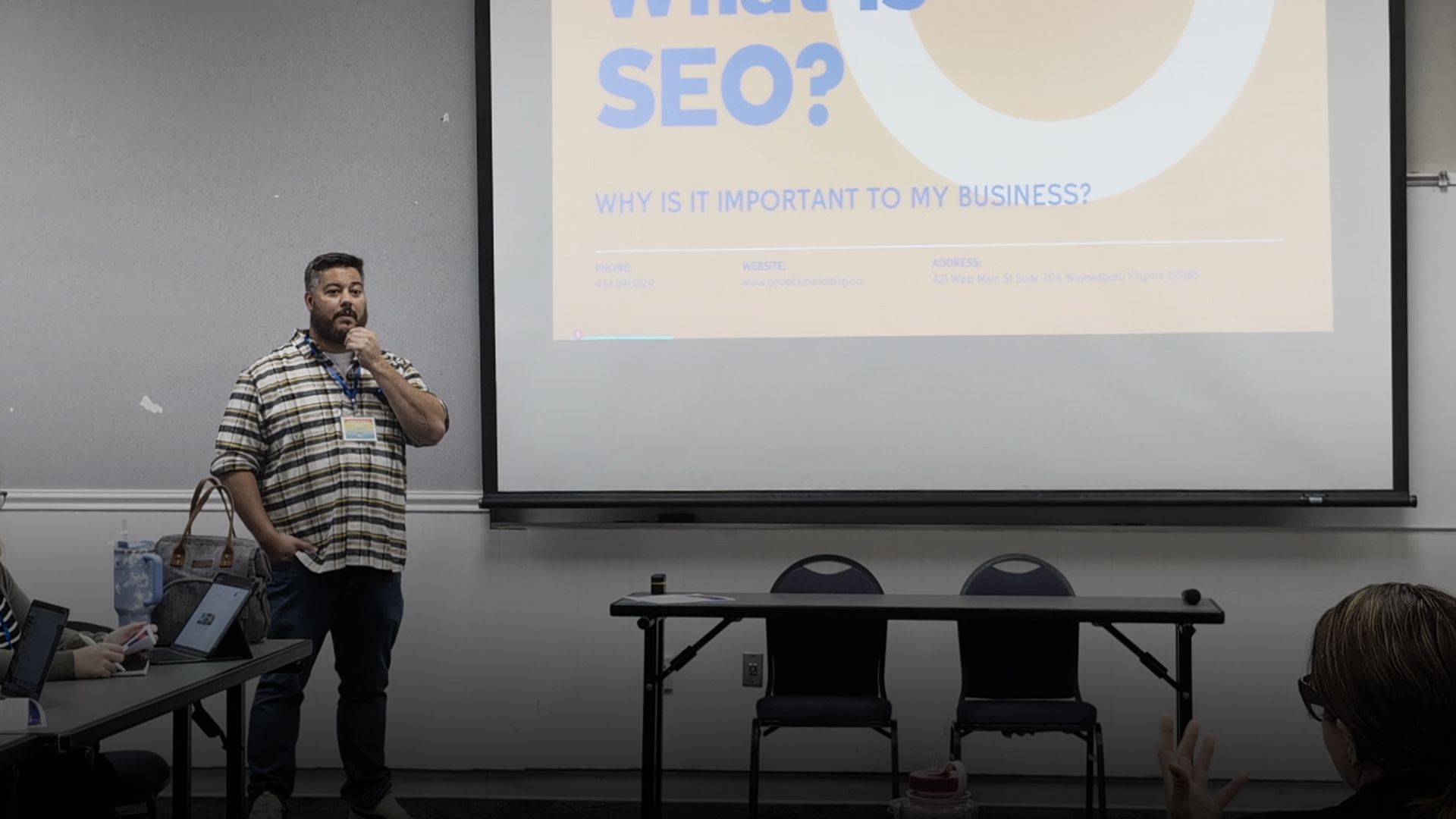 A man is giving a presentation in front of a projector screen in a classroom.