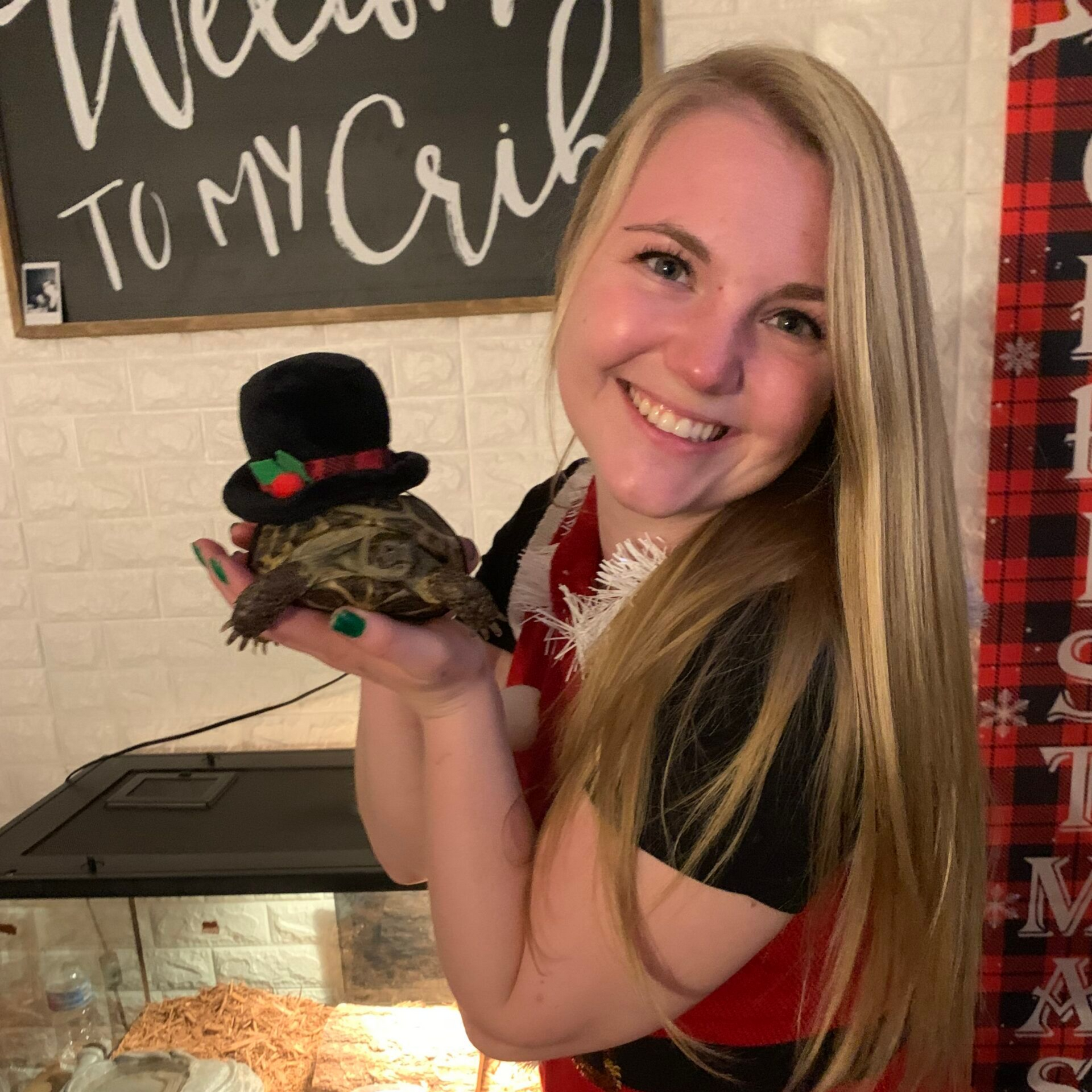Woman holding a turtle wearing a top hat. She smiles, with a festive setting.