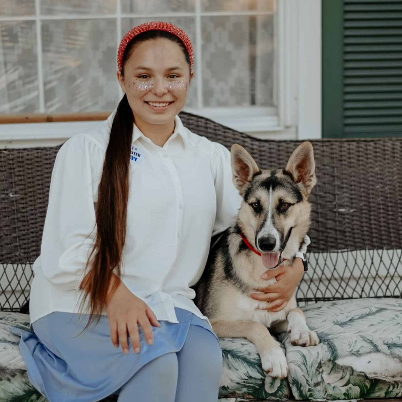 Woman with long hair and a dog sitting on a porch. The woman smiles, and the dog has its tongue out.