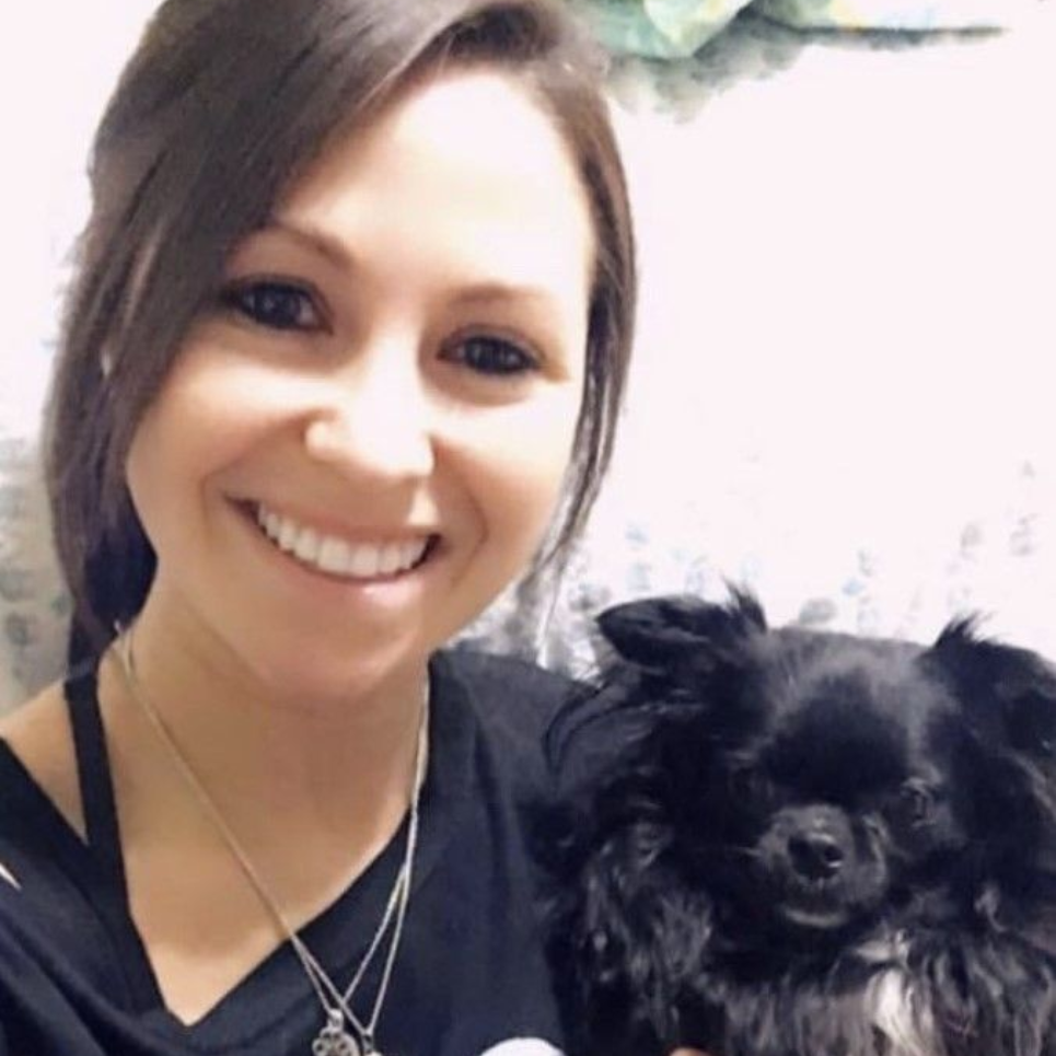 Woman smiling, holding a small, fluffy black dog; both looking at the camera.
