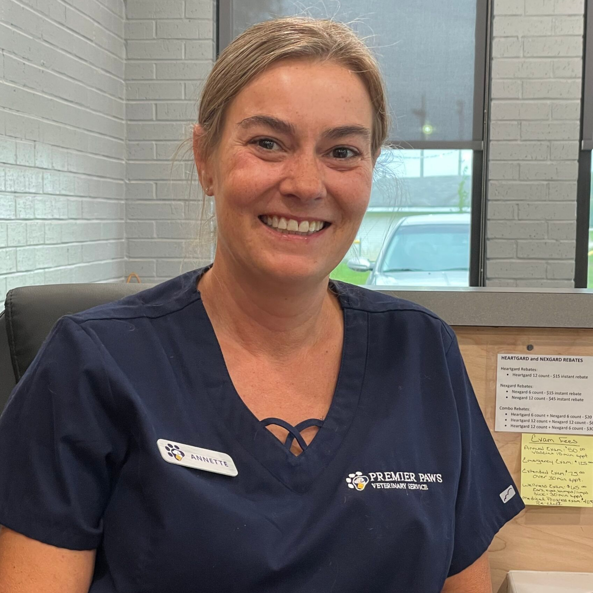 Woman in blue scrubs smiles at the camera in an office setting.