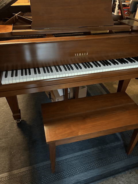 a piano is sitting on a wooden floor next to a bench .