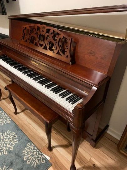 a piano is sitting on a wooden floor next to a bench .