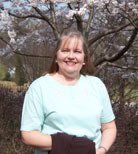 a woman in a light blue shirt is standing in front of a cherry blossom tree .