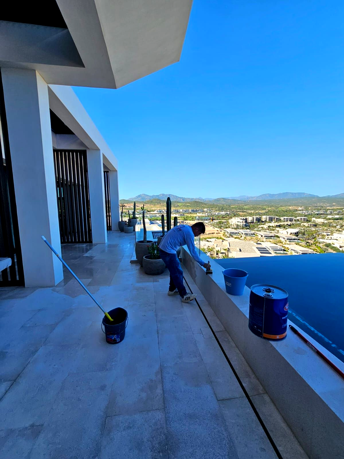 Man working on kitchen island in modern kitchen. Two others in the background. Beige and gold tones.