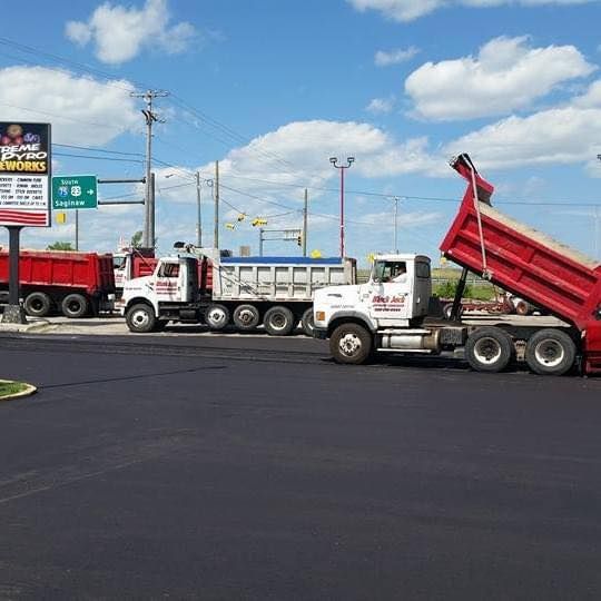 Asphalt paving in progress: dump trucks unloading black asphalt onto the road under a blue sky.