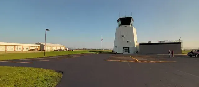 Airport control tower with attached building, asphalt, grass, buildings, and a clear blue sky.