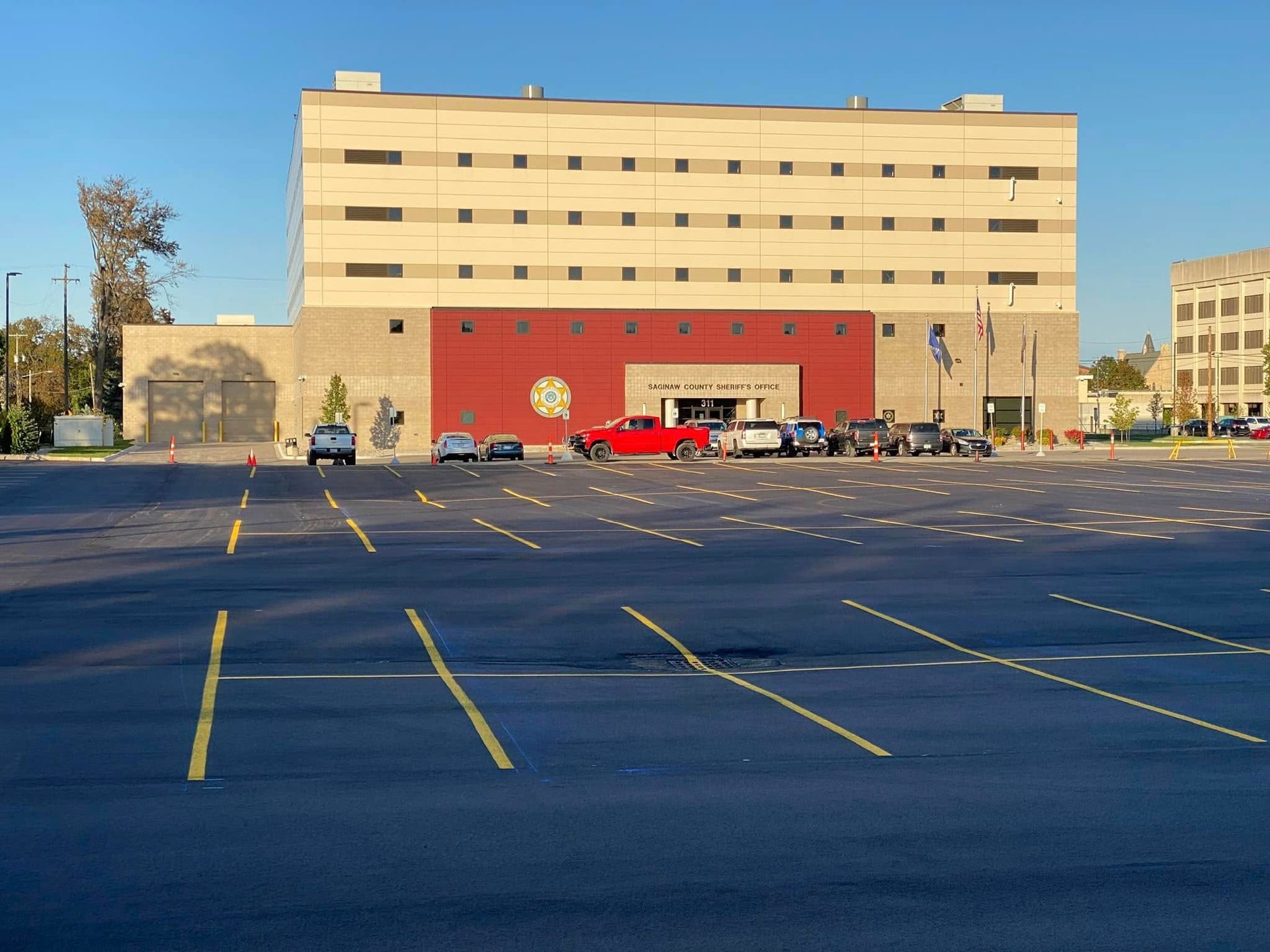 Exterior view of a multi-story building with a large parking lot. Red and tan brick facade, cars parked in front.