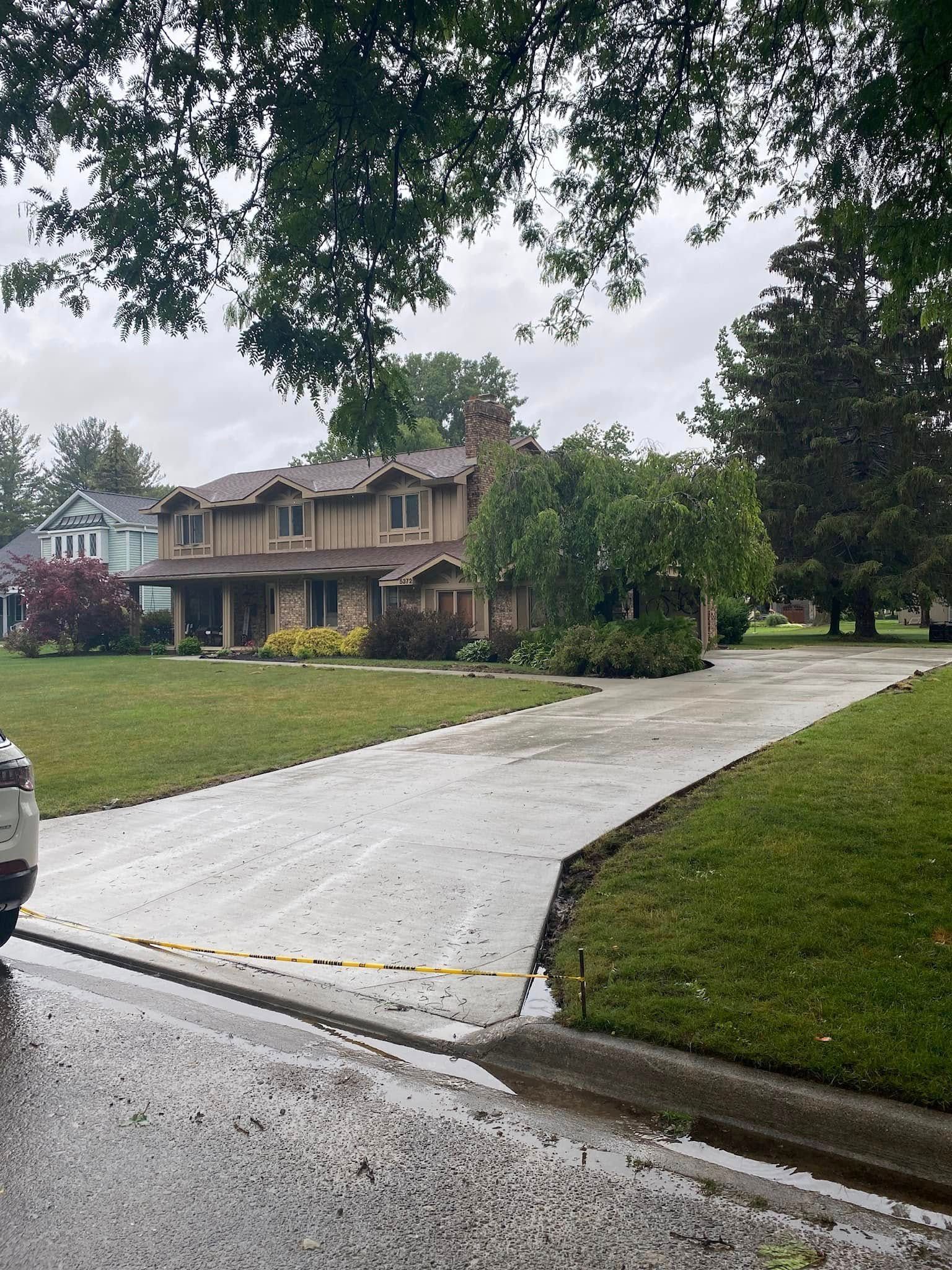 Driveway leading to a large house with a tan exterior and lush green lawn on a cloudy day.
