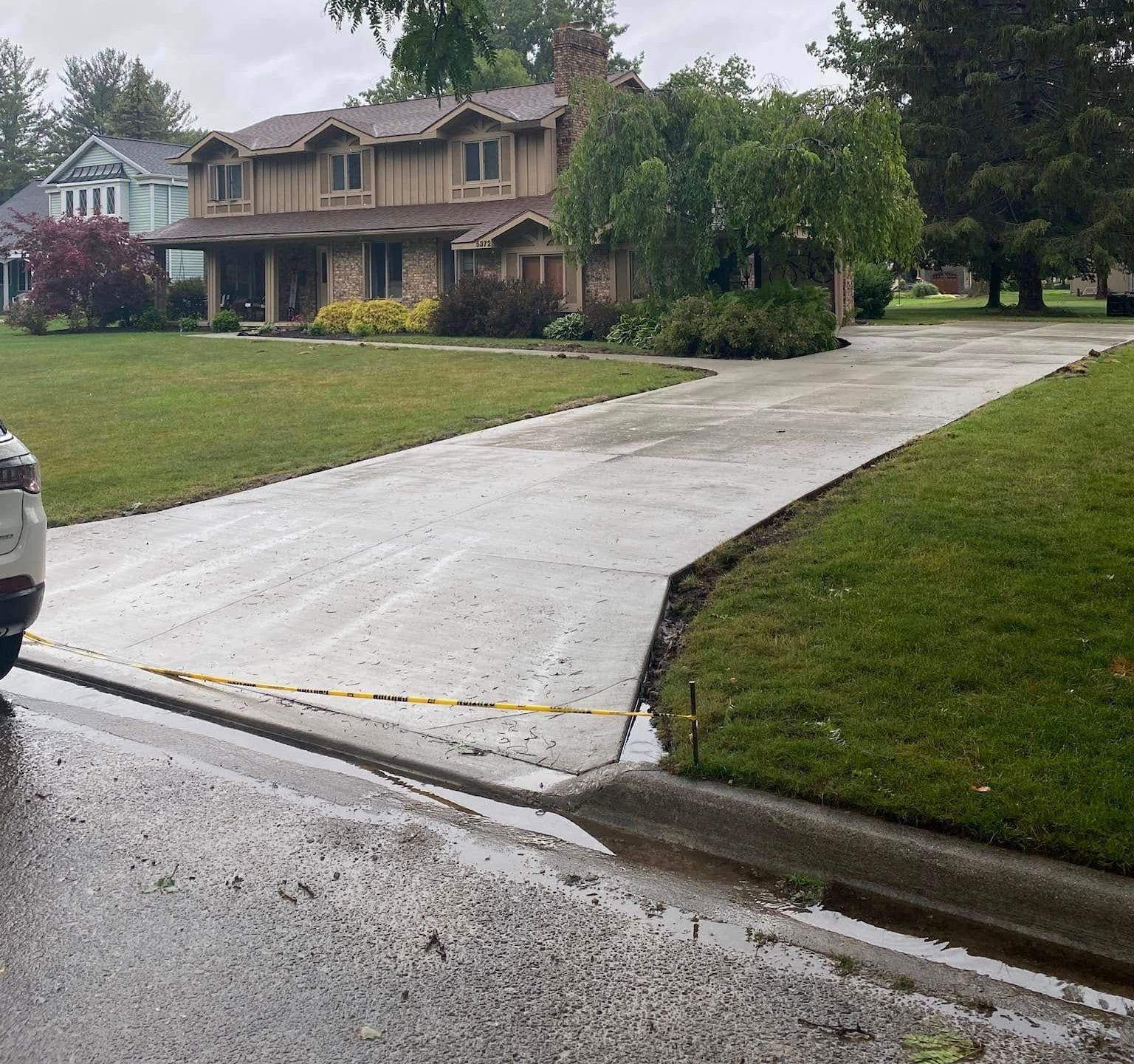 Driveway leading to a large house with a tan exterior and lush green lawn on a cloudy day.