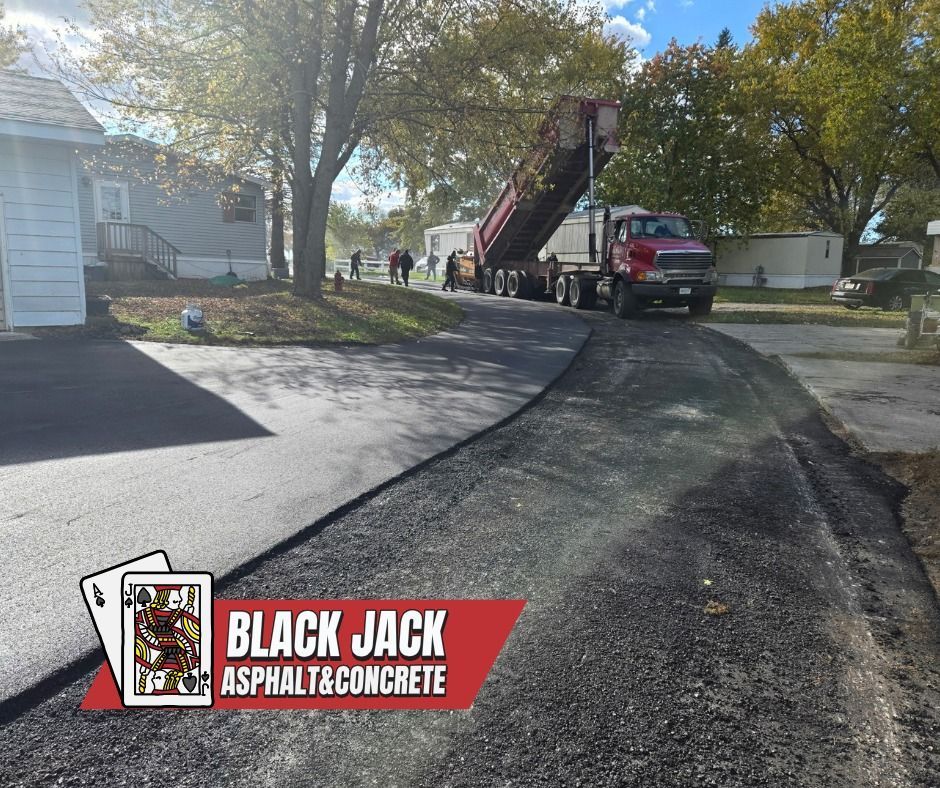 Asphalt paving, dump truck unloading asphalt on driveway. Black Jack Asphalt & Concrete logo.