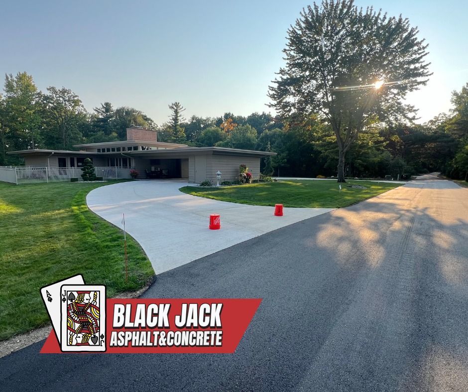 Newly paved driveway in front of a modern home, with the logo for Black Jack Asphalt & Concrete in the bottom left.