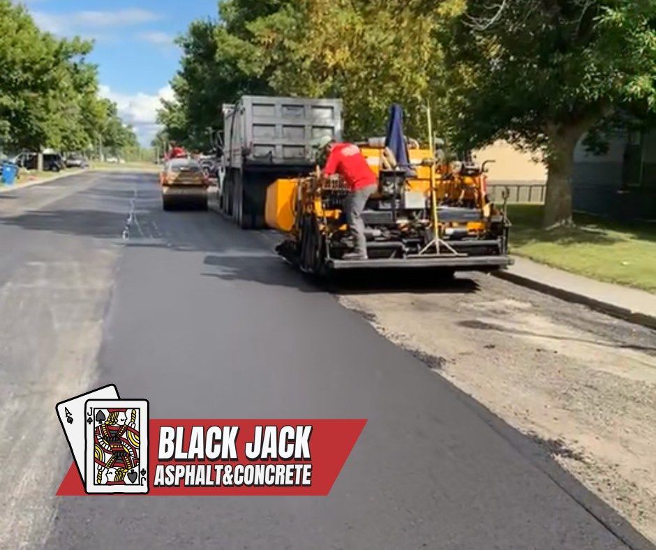 Asphalt paving in progress on a street. Blacktop machine, dump truck, and worker.