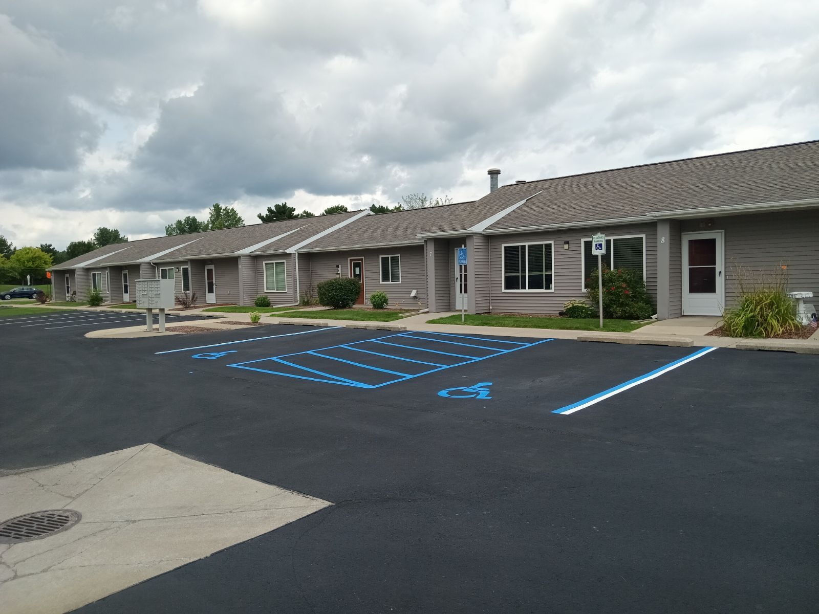 Newly paved black asphalt parking lot next to a gray concrete sidewalk; Black Jack Asphalt & Concrete logo.