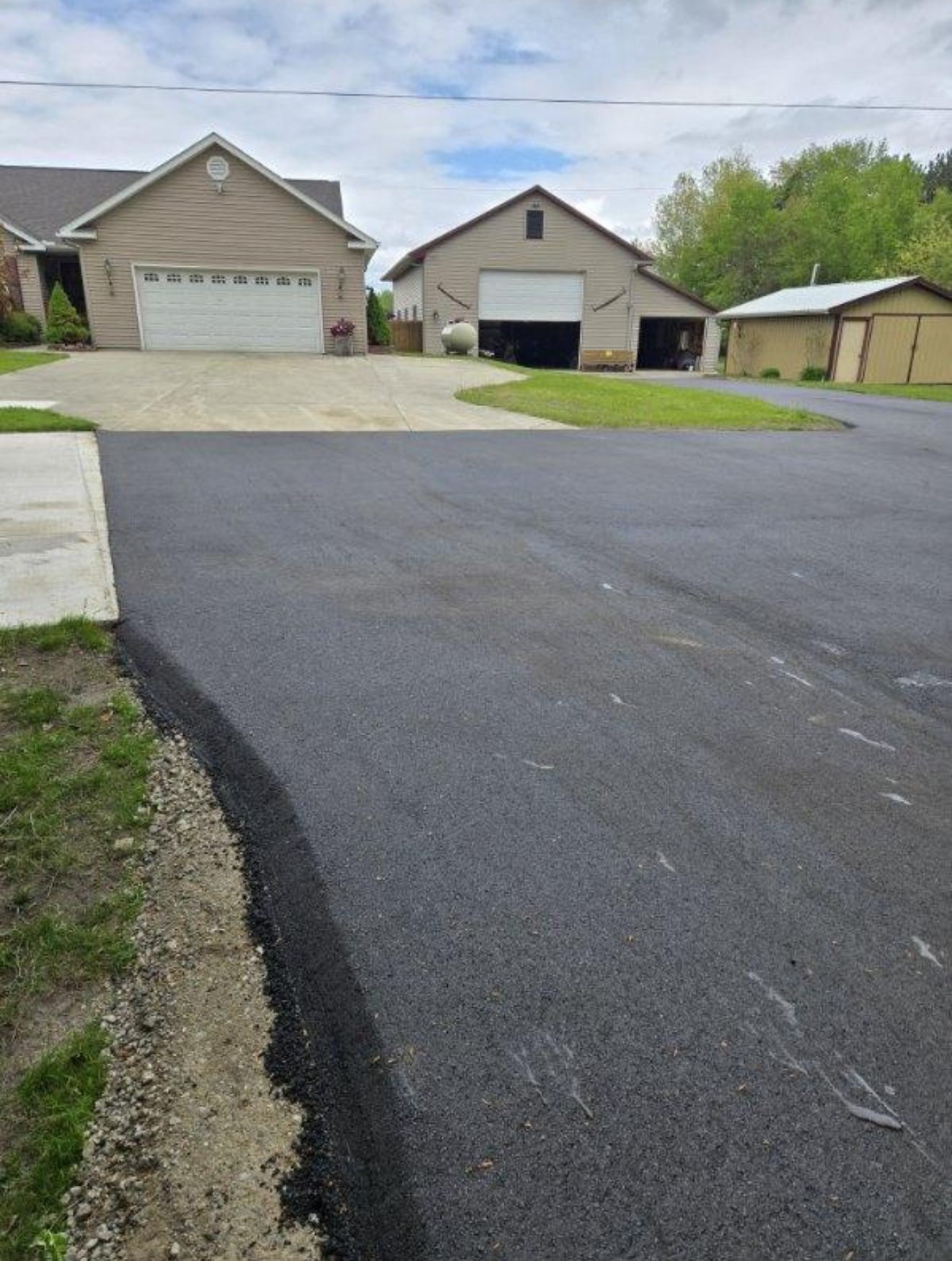 Asphalt path through green park, leading to a field.