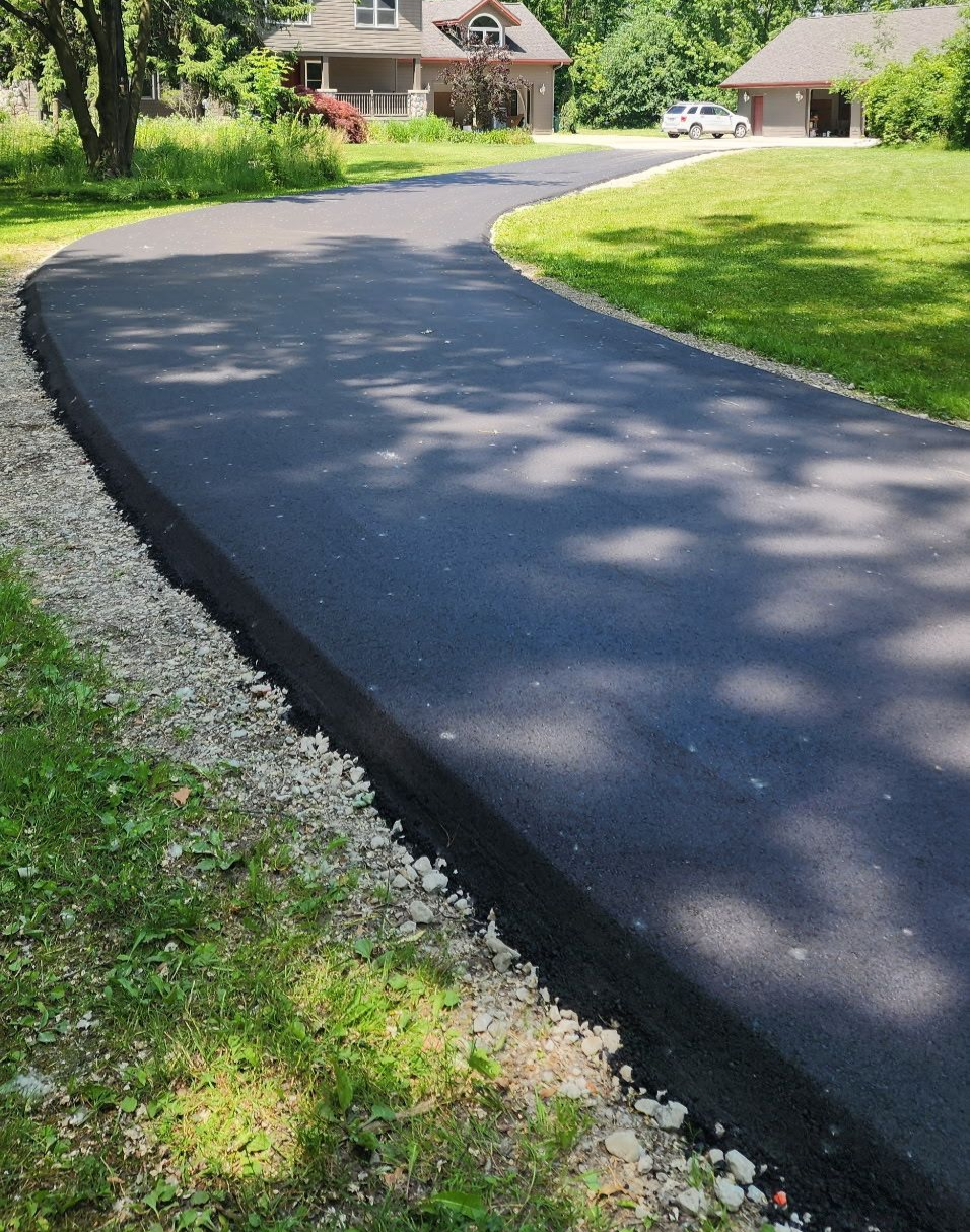 Asphalt paving crew at work, truck dumping asphalt onto paver in a cemetery, sunny day.