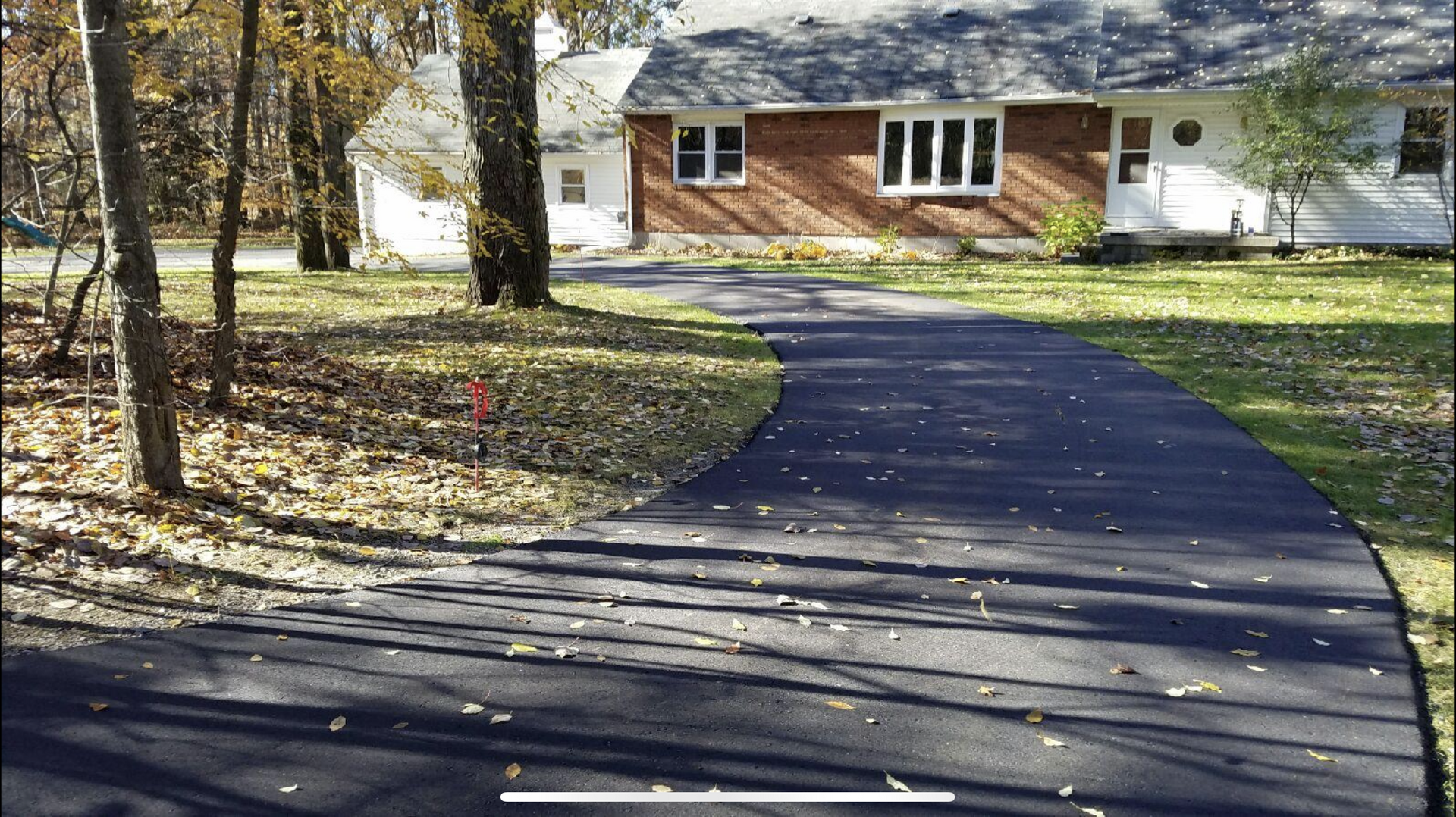 Brown house with a brick-like walkway, lawn, and two white chairs on a patio.