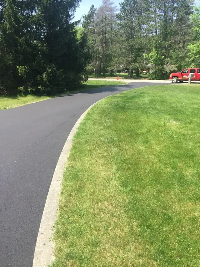 Black asphalt driveway curves through green lawn; red pickup truck parked on the right.