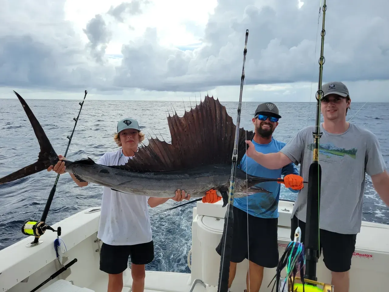 Three men are standing on a boat holding a sailfish.