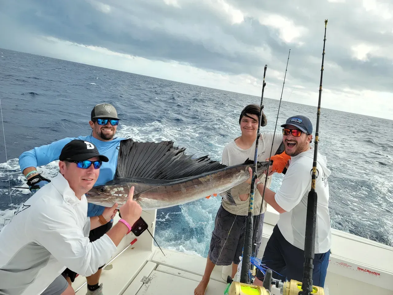 A group of people are standing on a boat holding a sailfish.