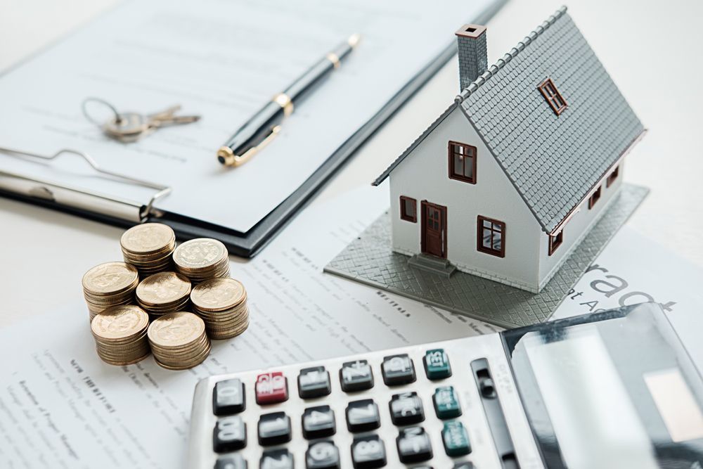 A model house is sitting on top of a pile of coins next to a calculator.