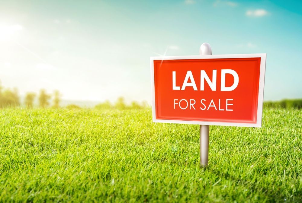 A red and white land for sale sign in a grassy field.