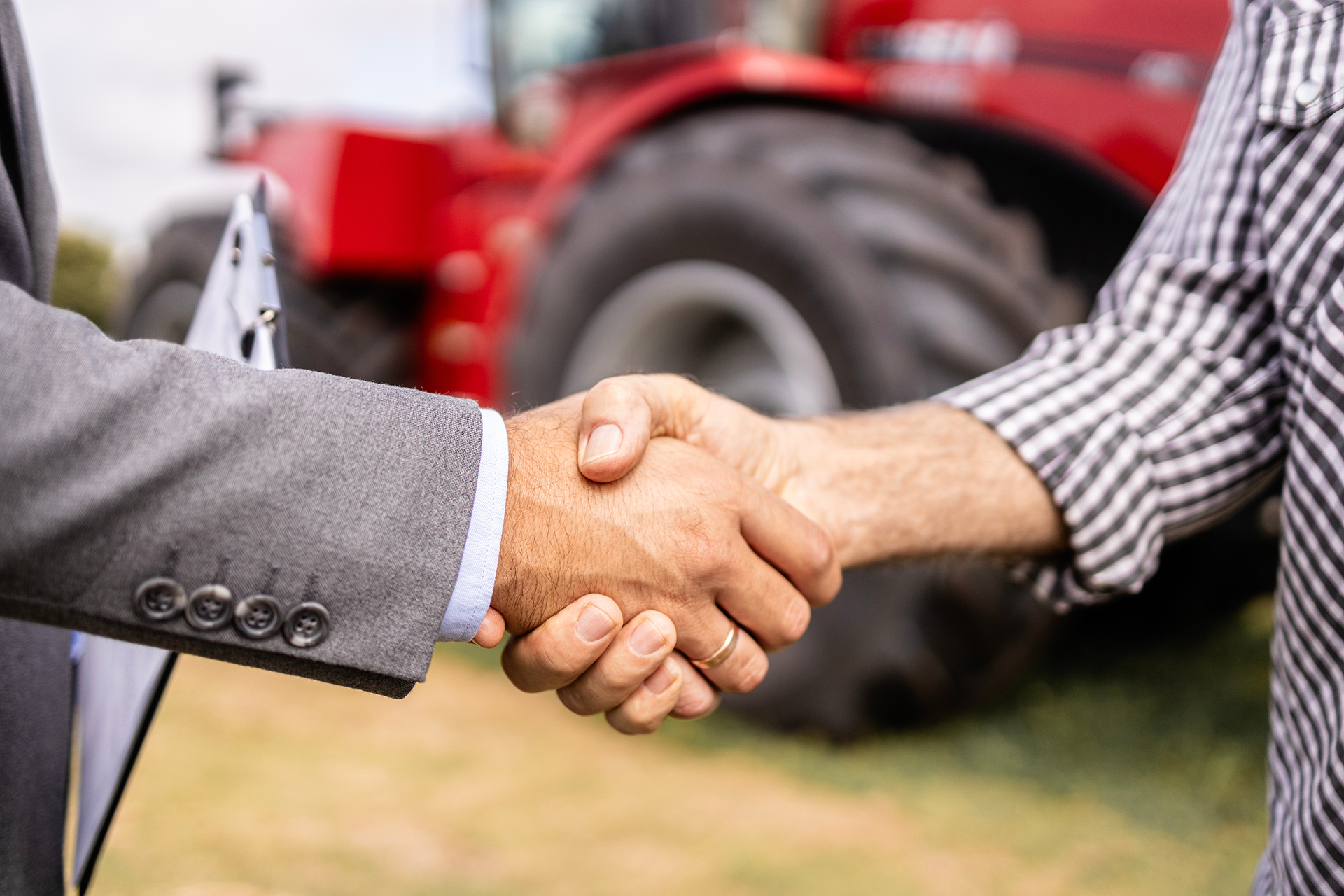 Two men are shaking hands in front of a red tractor.
