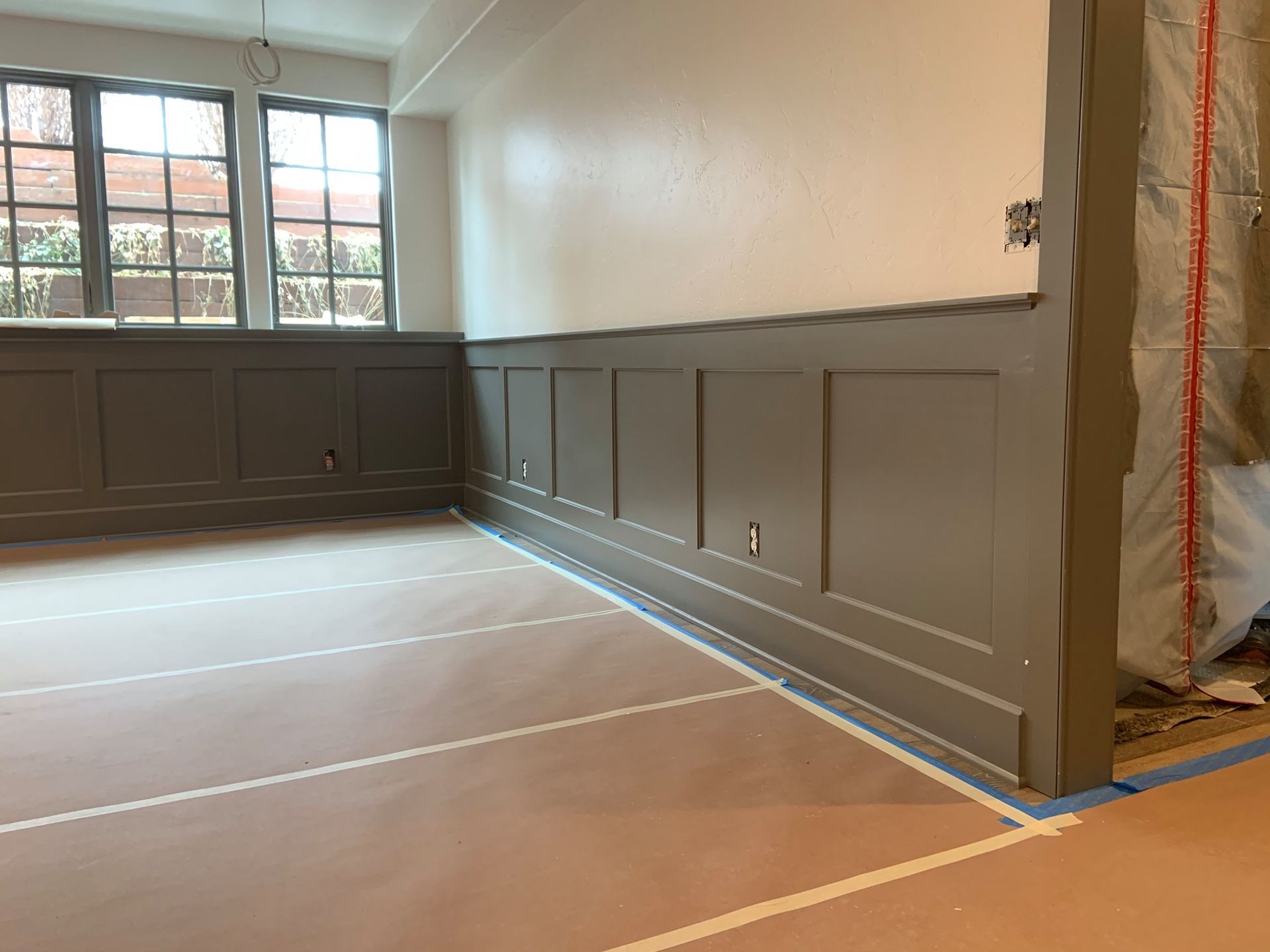 A room with a gray wall and a blue tape on the floor.