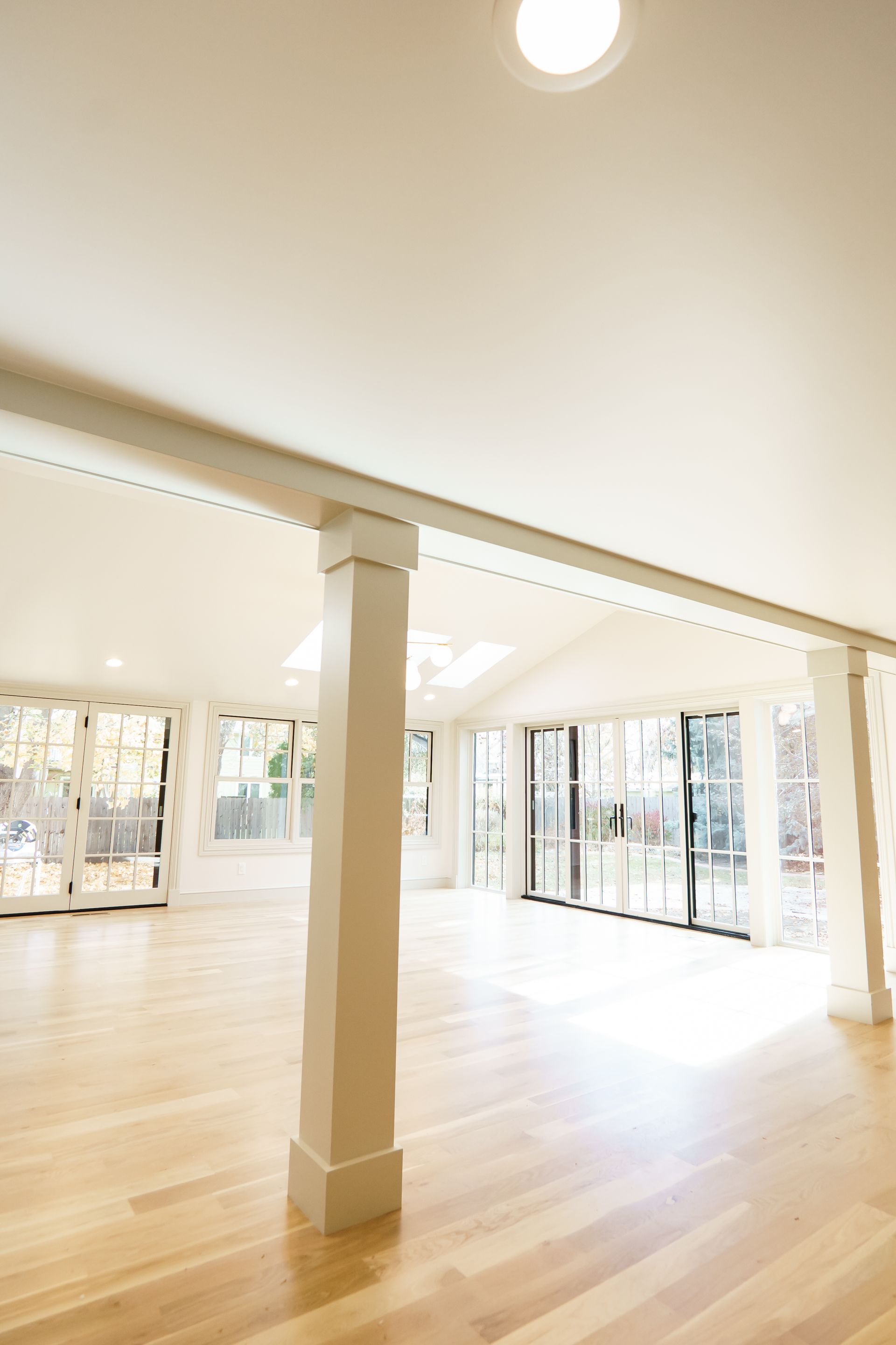 A large empty room with hardwood floors and white pillars.
