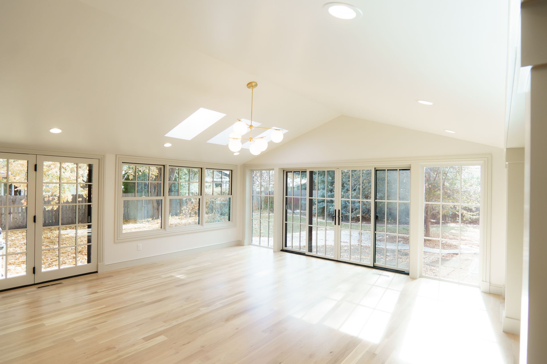 An empty living room with lots of windows and hardwood floors.