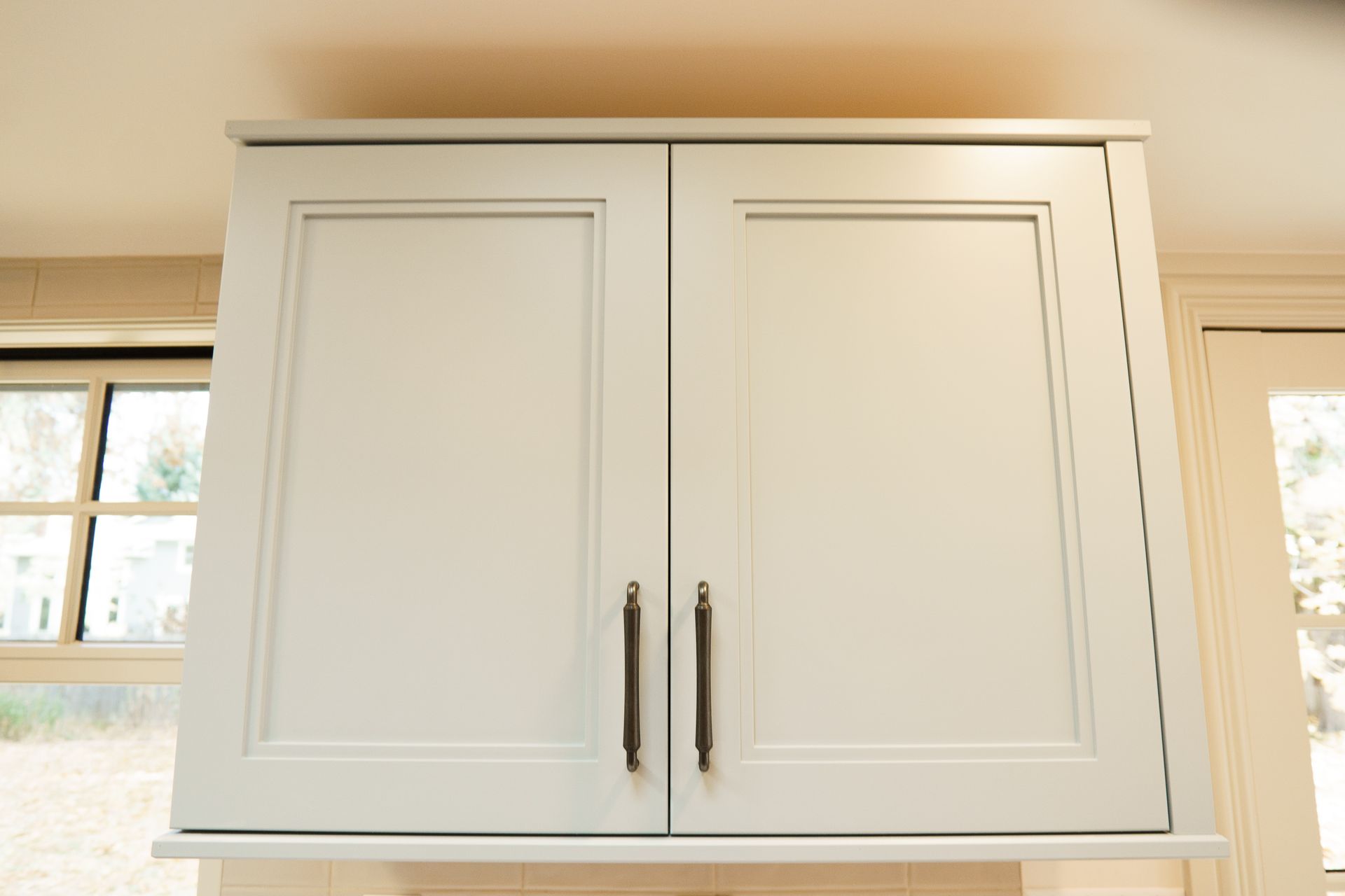 A white cabinet with two doors is hanging from the ceiling in a kitchen.