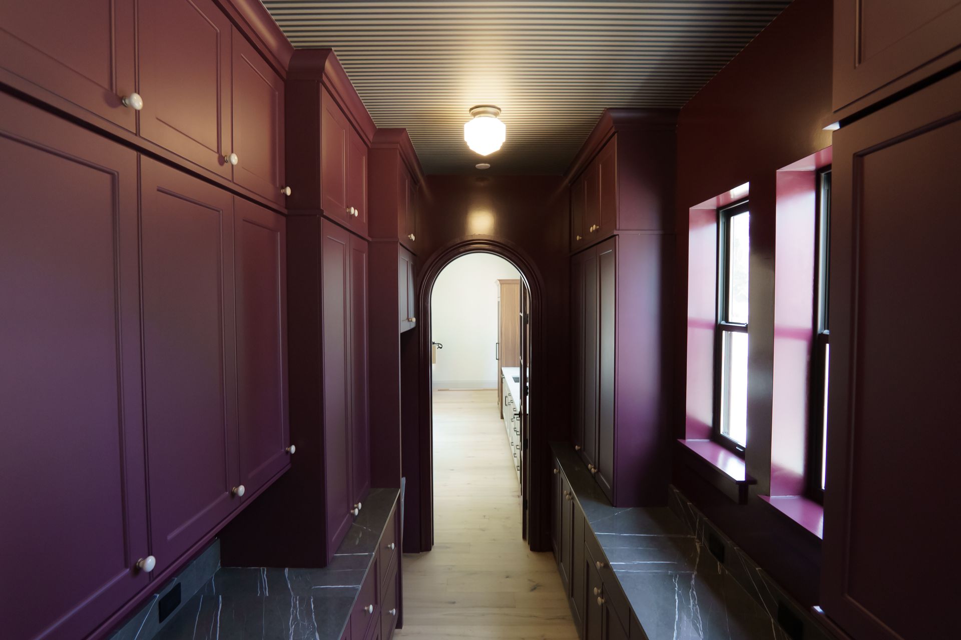 A long hallway with purple cabinets and windows leading to a kitchen.