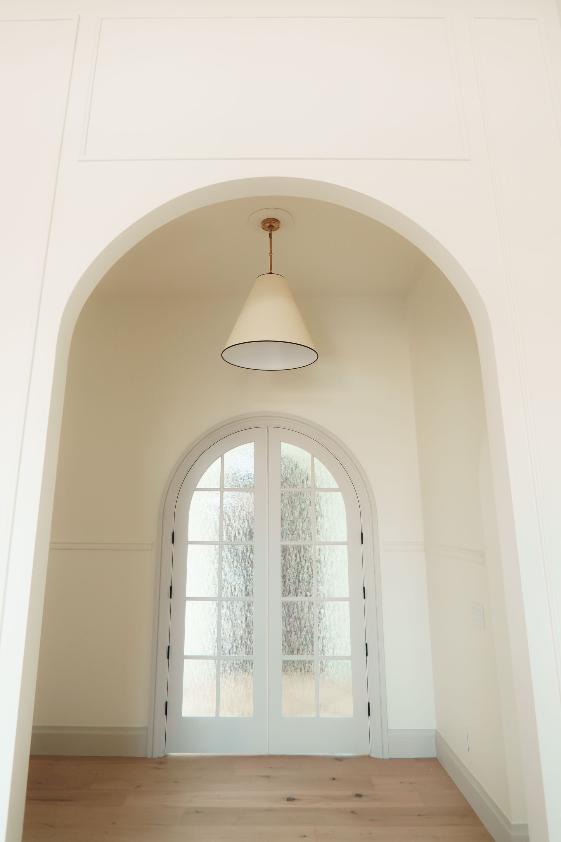 A hallway with arched doors and a light hanging from the ceiling.