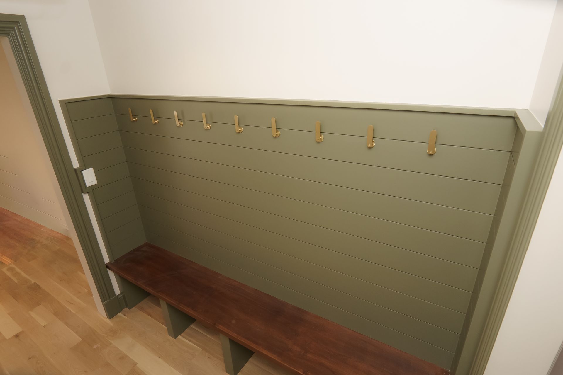 A wooden bench in a hallway next to a wall with hooks