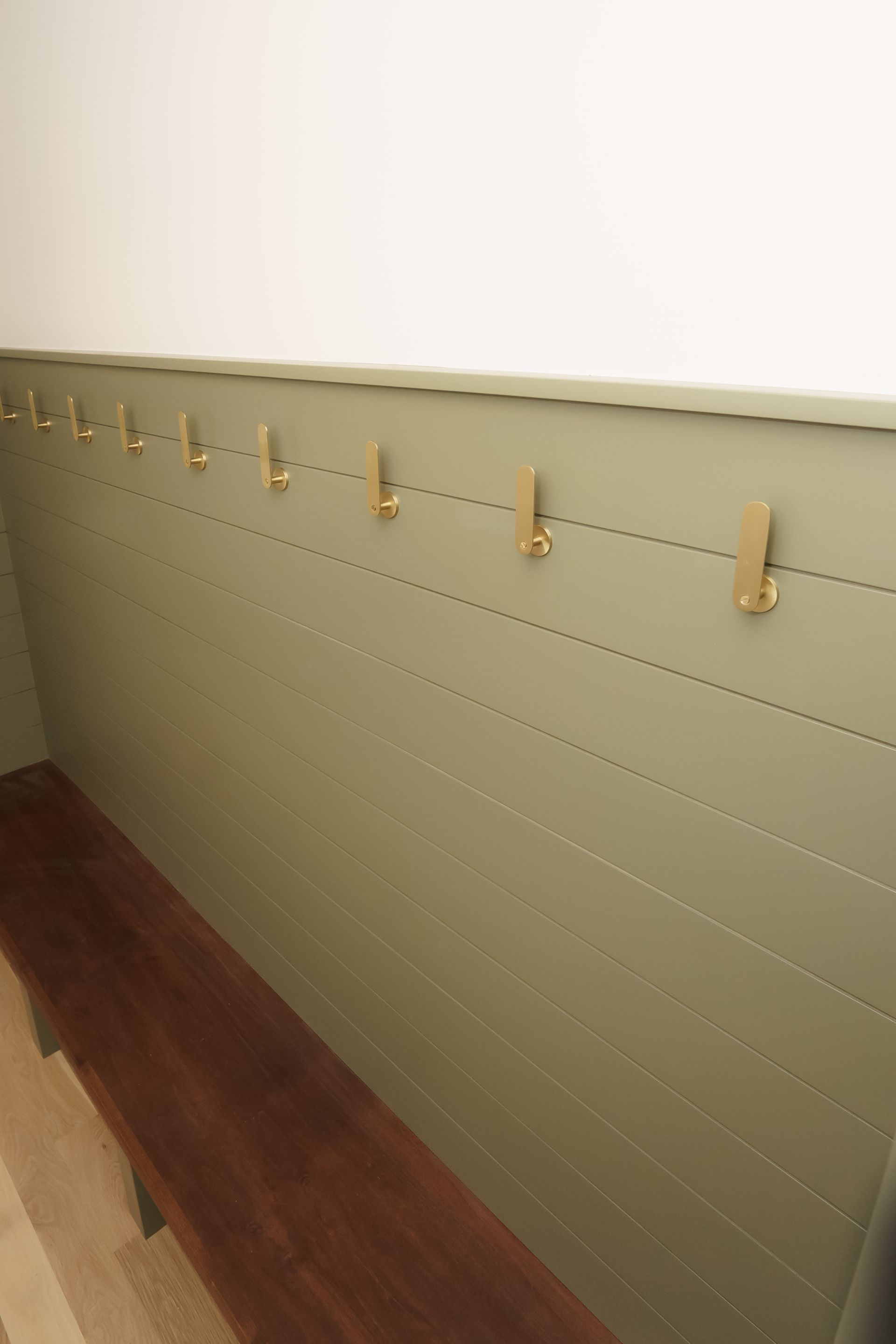 A wooden bench is sitting in front of a wall with hooks on it.