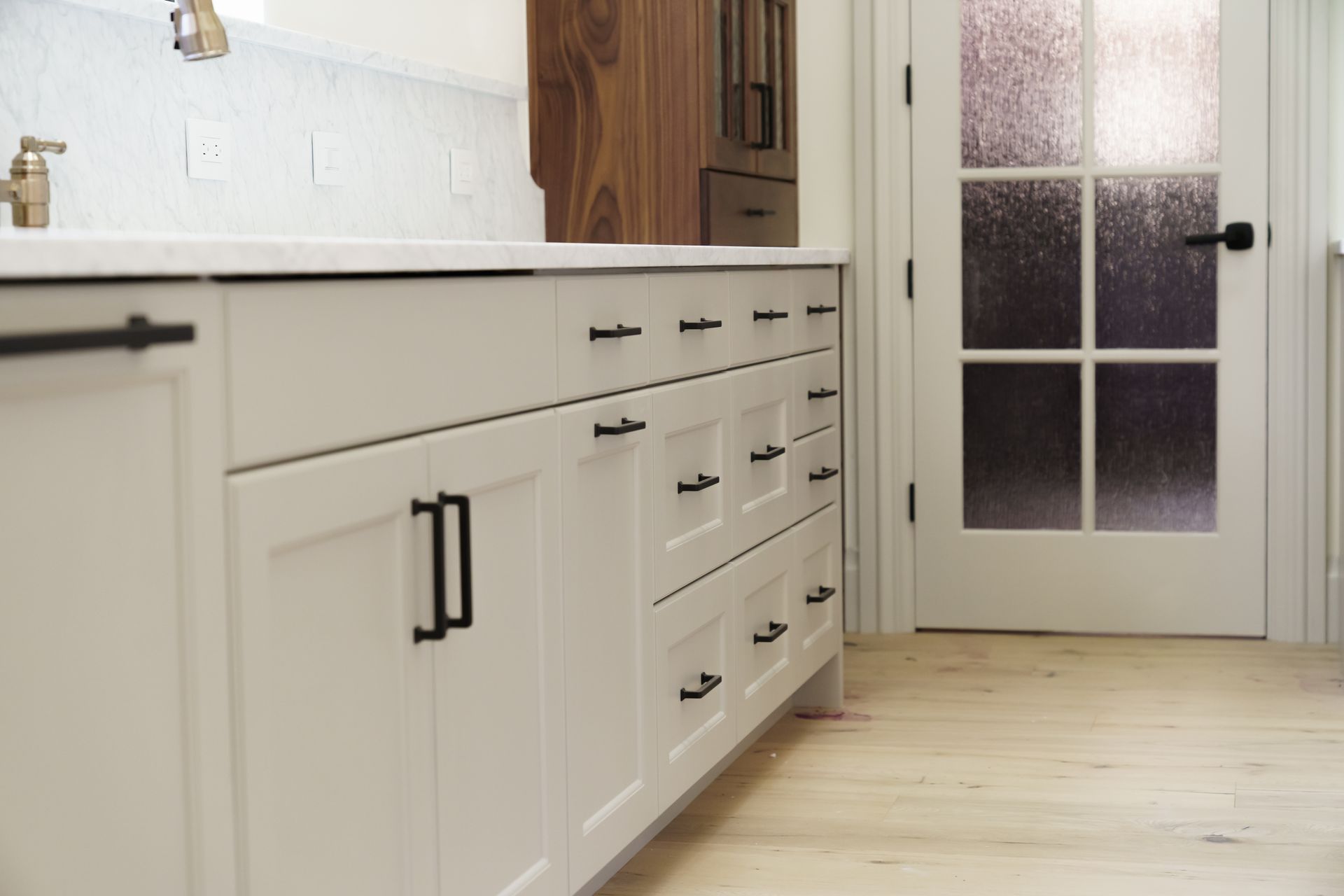 A kitchen with white cabinets and black handles and a glass door.