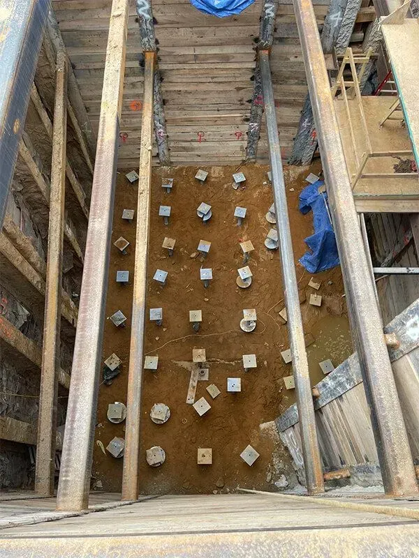 Construction site with wooden supports and metal beams. Excavated earth with evenly spaced, concrete posts.