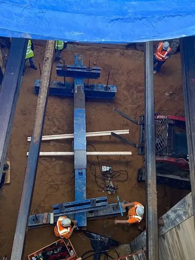 Construction workers operating machinery in a dirt pit, under a blue tarp.