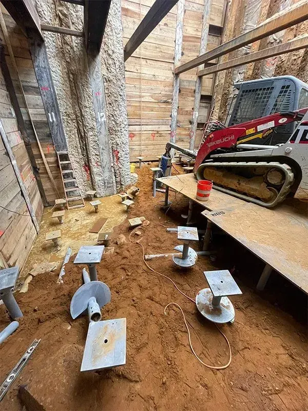 Construction site: Helical piers being installed. A small skid steer next to the wall.
