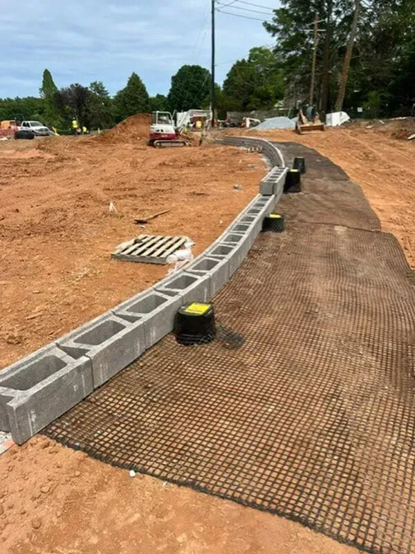Construction site with concrete blocks forming a curb. Black grid fabric covers the ground.