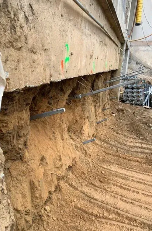 Construction site with exposed concrete wall and metal rods, soil below.