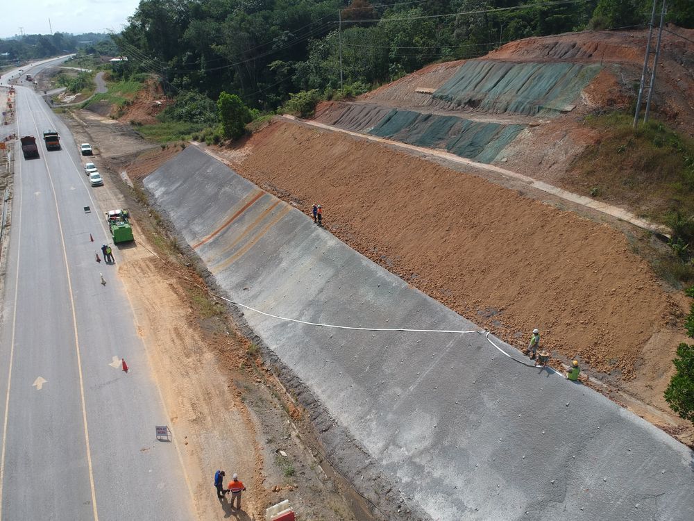 Highway construction site with retaining wall being built; workers, trucks, earth.