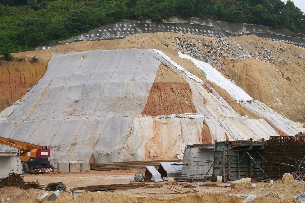 Construction site with layers of soil and covering, crane, and shed.