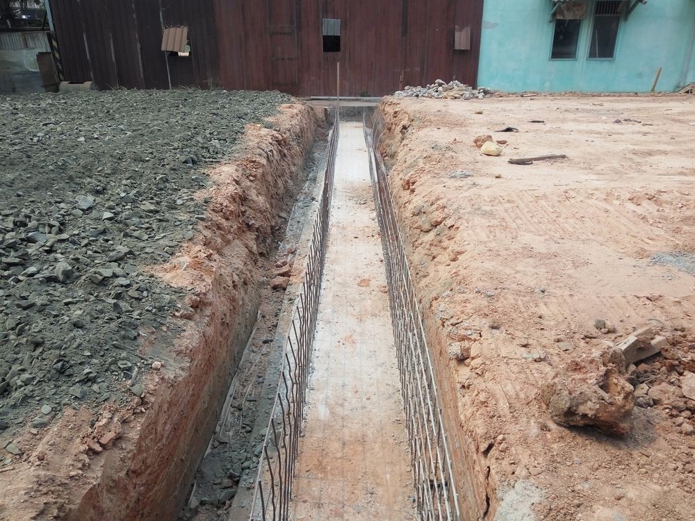 A long, narrow trench dug in dirt and gravel; bricks line the trench walls.