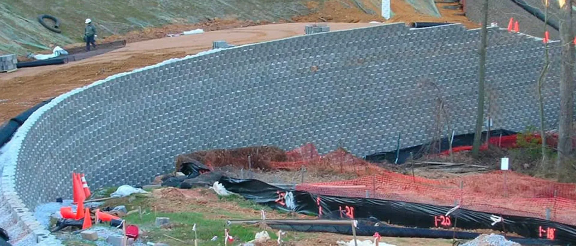 Construction site with large retaining wall, dirt, and an excavator.